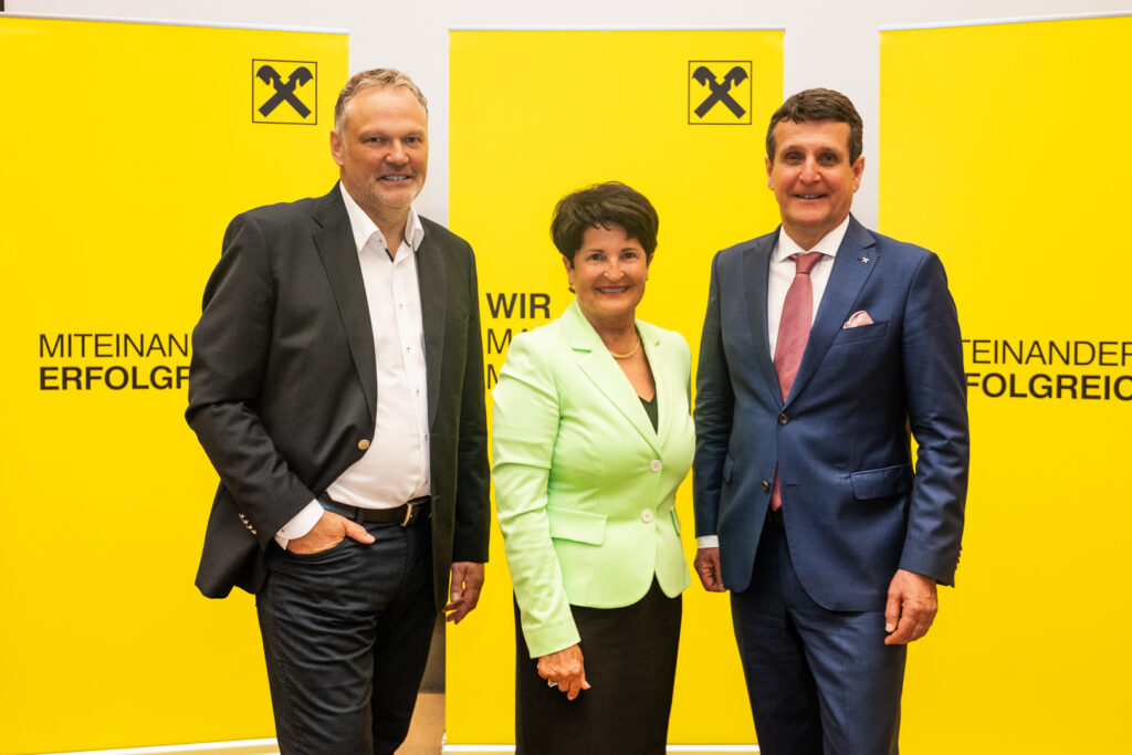 Zwei Herren und eine Dame in eleganter Kleidung vor gelbem Hintergrund.