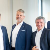 Sechs Herren in Anzügen stehen in einer Bank.
