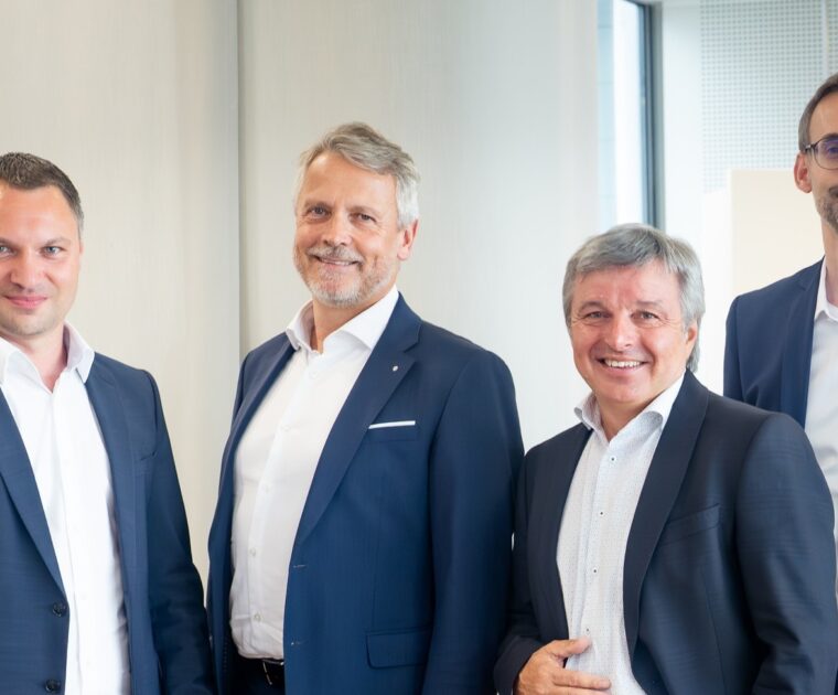 Sechs Herren in Anzügen stehen in einer Bank.