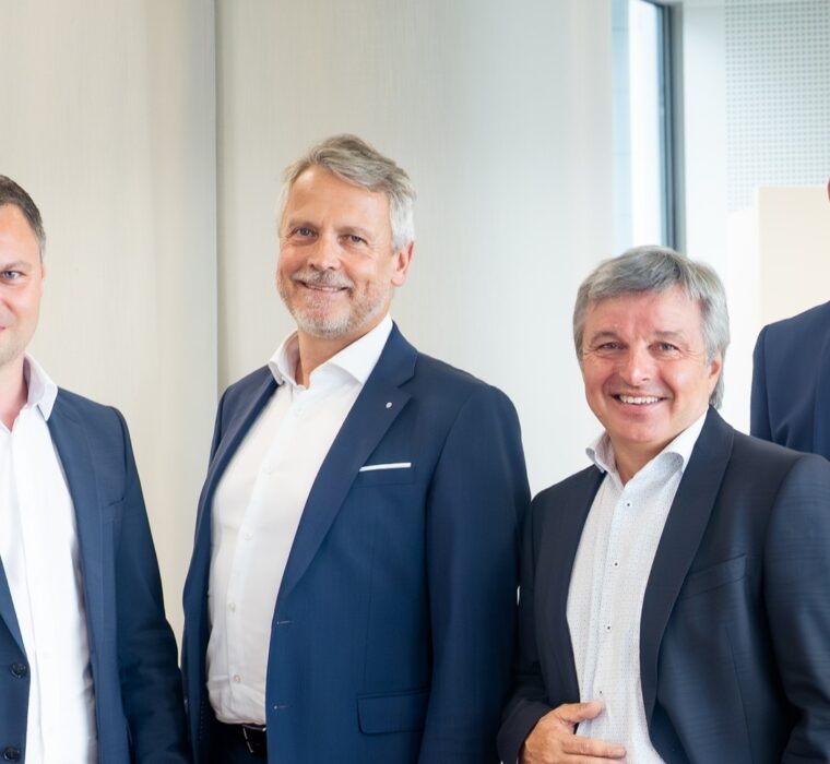 Sechs Herren in Anzügen stehen in einer Bank.