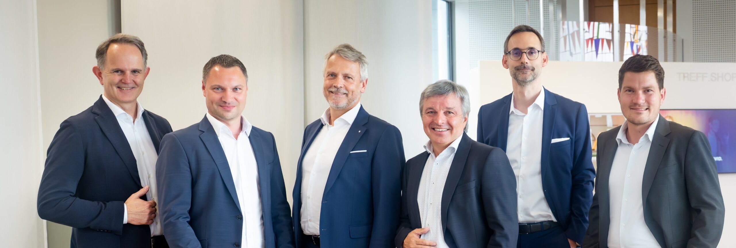Sechs Herren in Anzügen stehen in einer Bank.