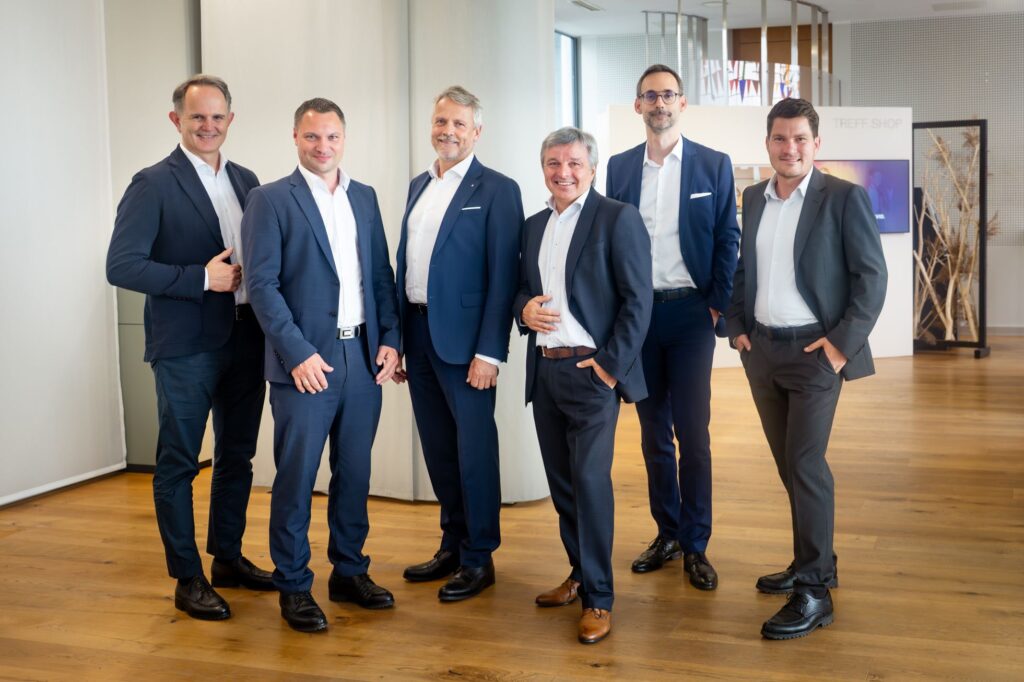 Sechs Herren in Anzügen stehen in einer Bank.